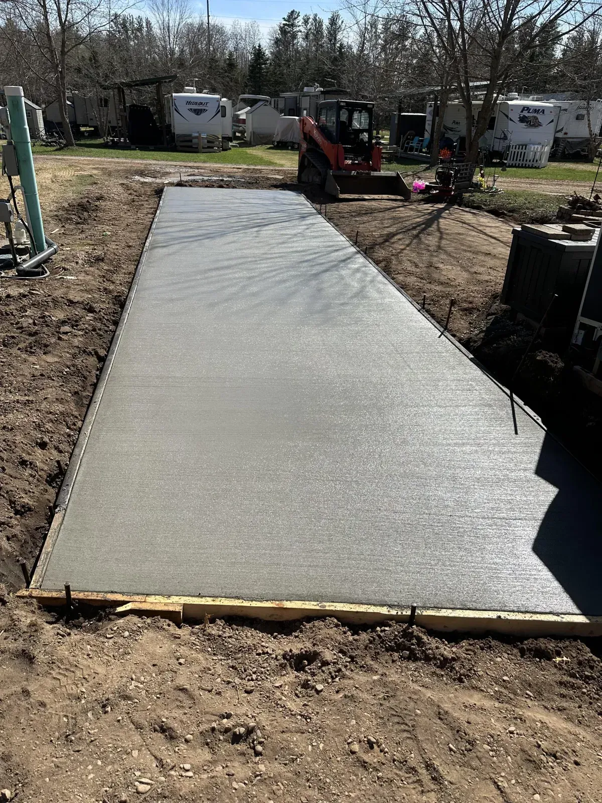 Freshly poured concrete walkway under construction with a skid steer nearby outdoors