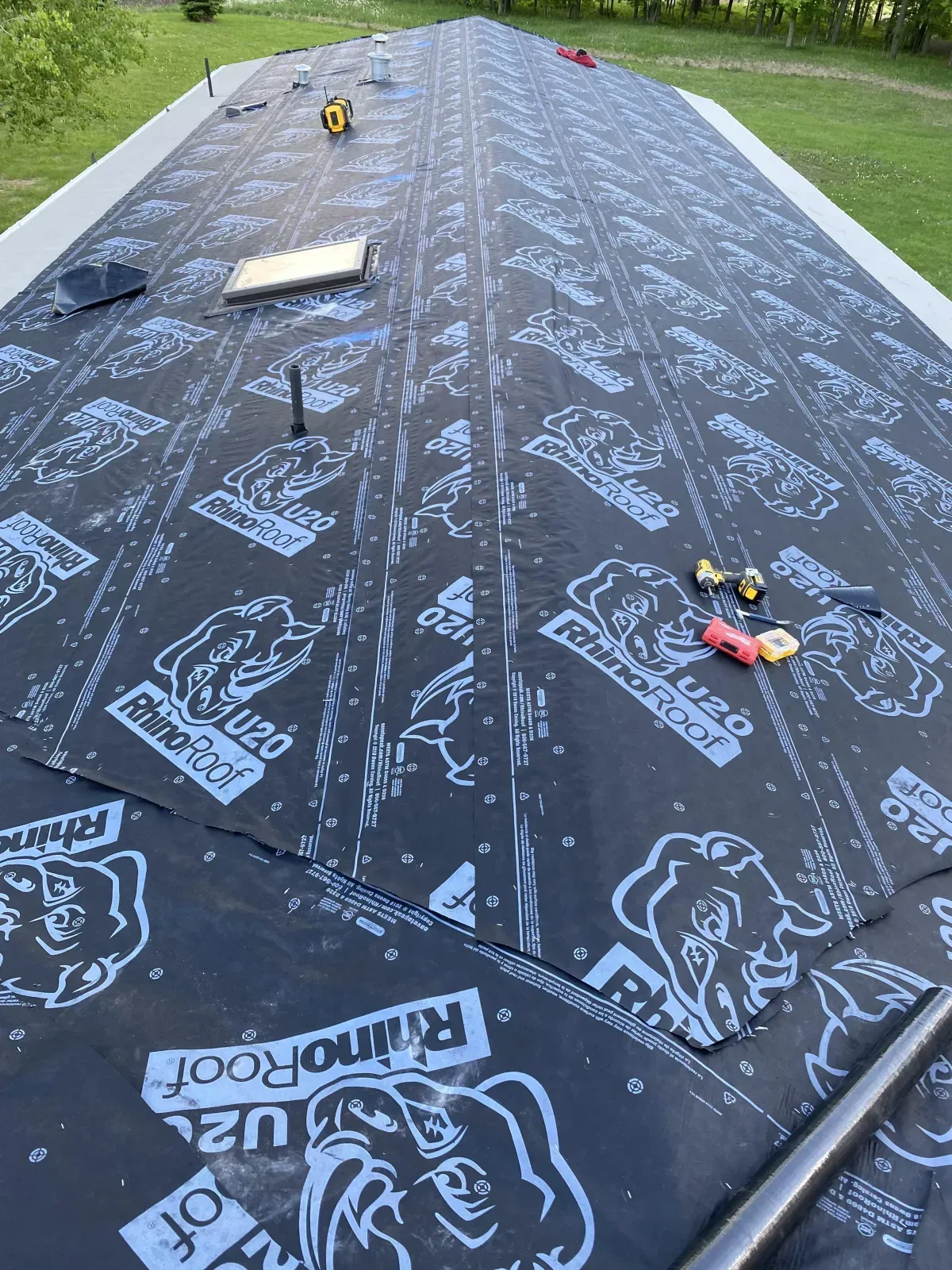 Roof underlayment installed on a sloped roof, with tools and materials scattered along the ridge.