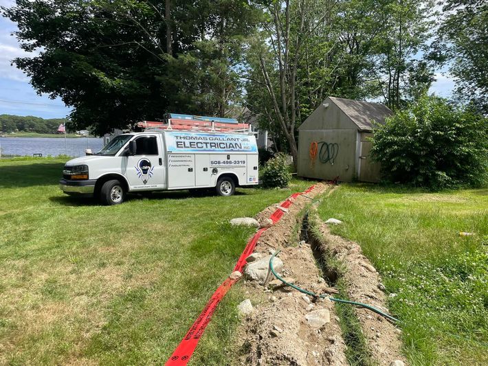 White work van parked on grass near a trench with a shed and water in the background.