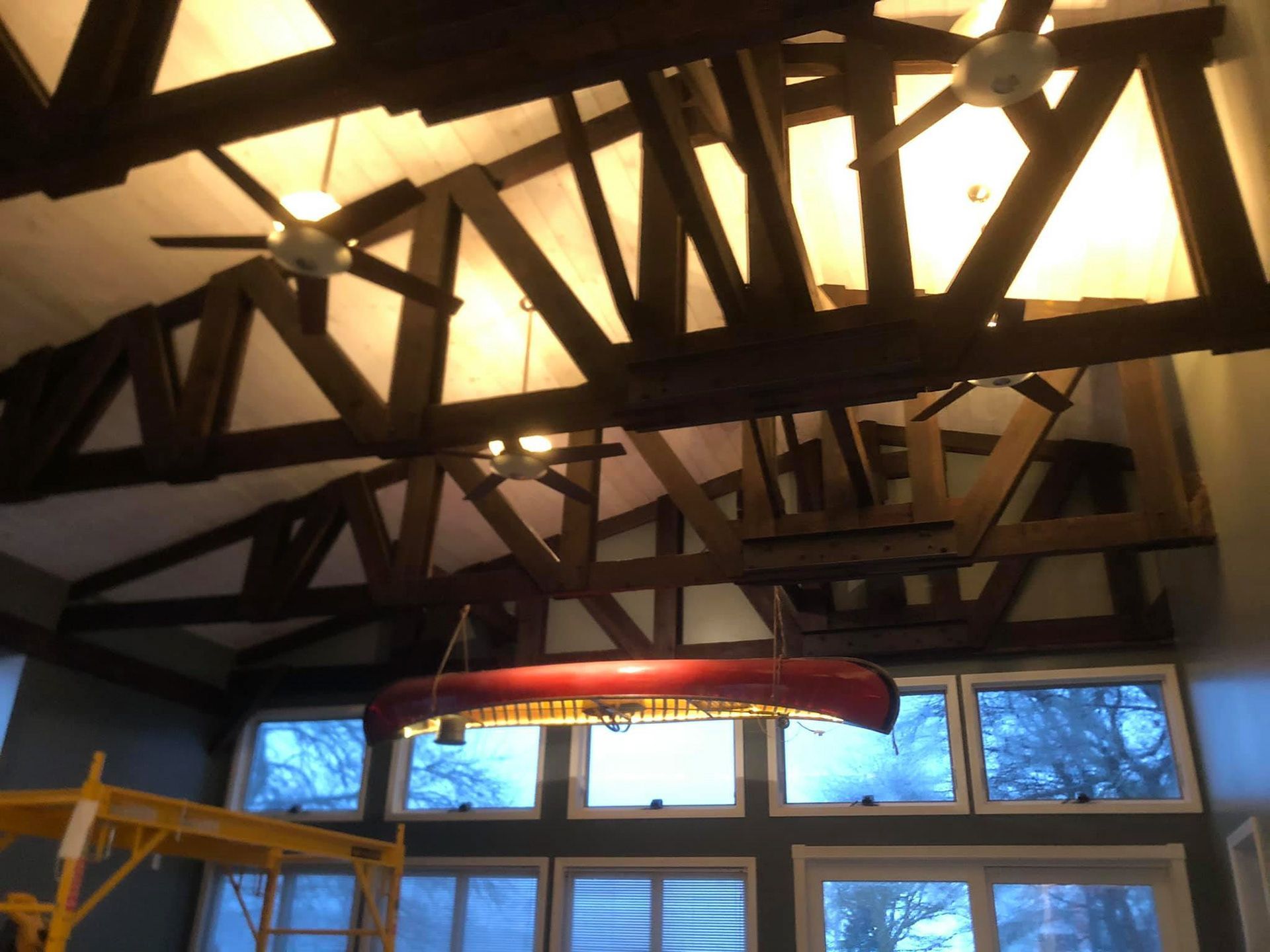 Wooden beams and a canoe suspended from a high ceiling over large windows.