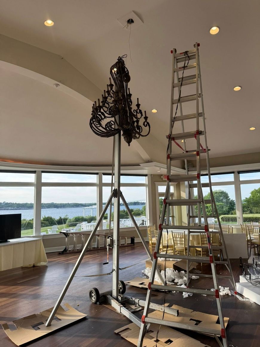 Chandelier being installed in a room with a view; a tall ladder and lift assist the process.