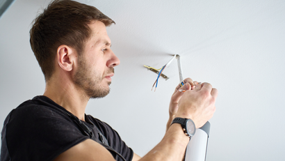 Man installing electrical wiring in a white ceiling with a screwdriver.