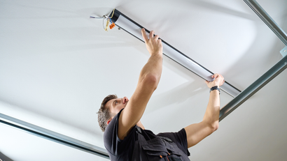 Person installing a fluorescent light fixture on a white ceiling.