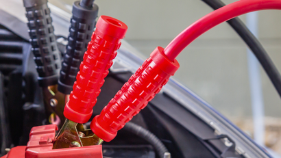 Red jumper cables attached to a car battery terminal, providing a jump start.