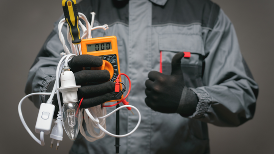 Electrician in work attire holding tools and giving a thumbs up.