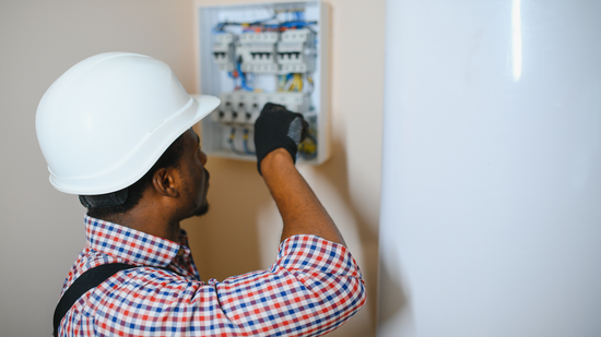 Electrician in a hard hat working on an electrical panel.