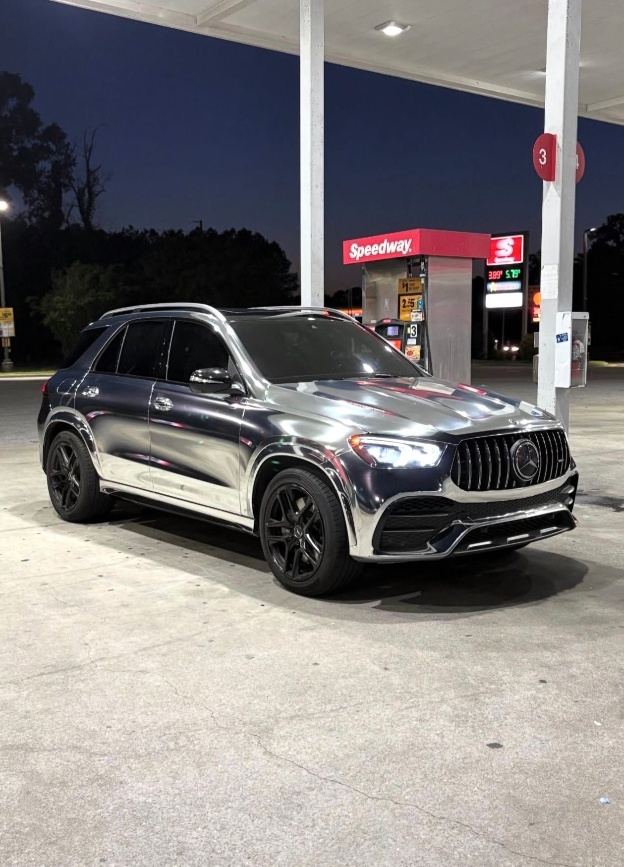 Dark gray SUV parked at a gas station at night under bright canopy lights.