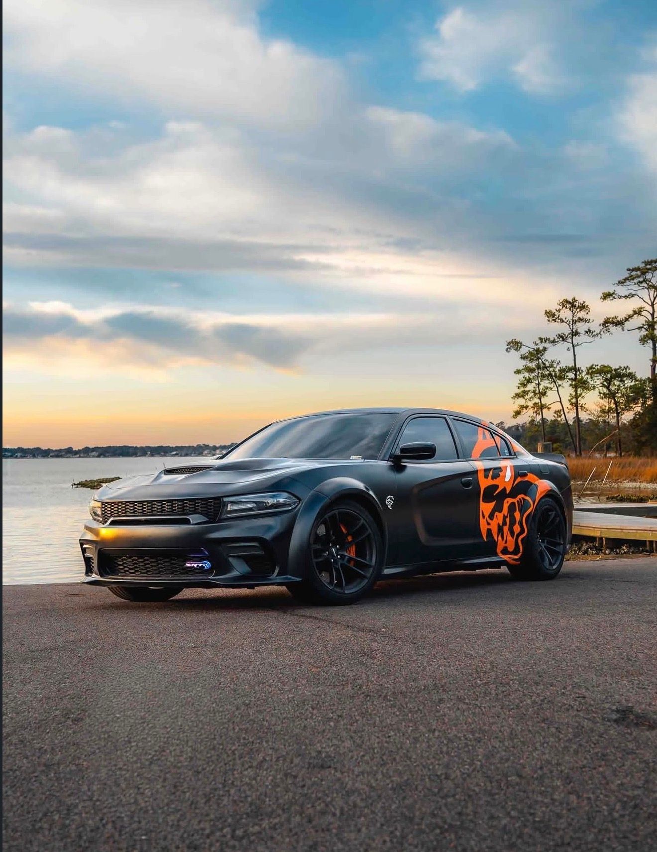 Black sports car with orange flame decals parked by a lakeside at sunset