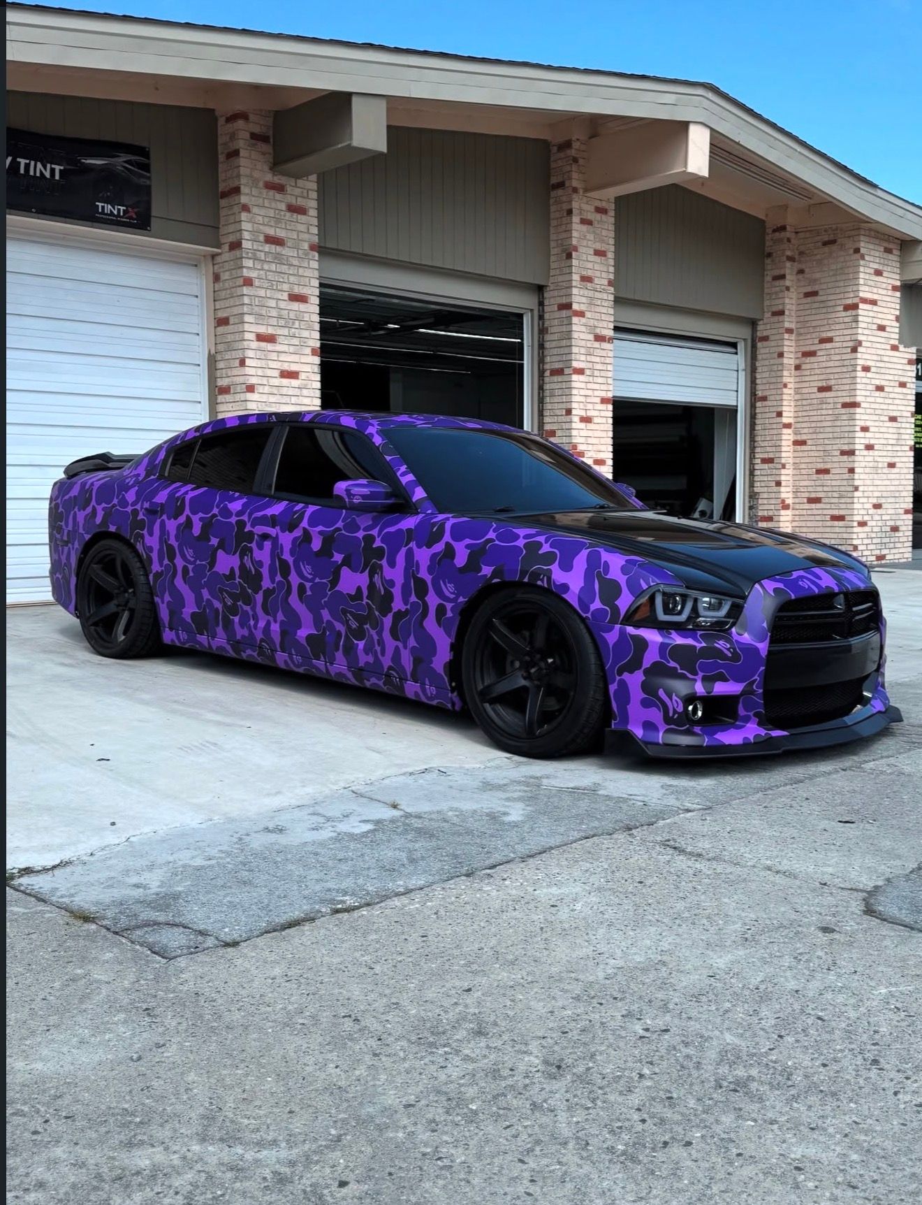 Purple camouflage sports car parked in front of a brick garage with white doors