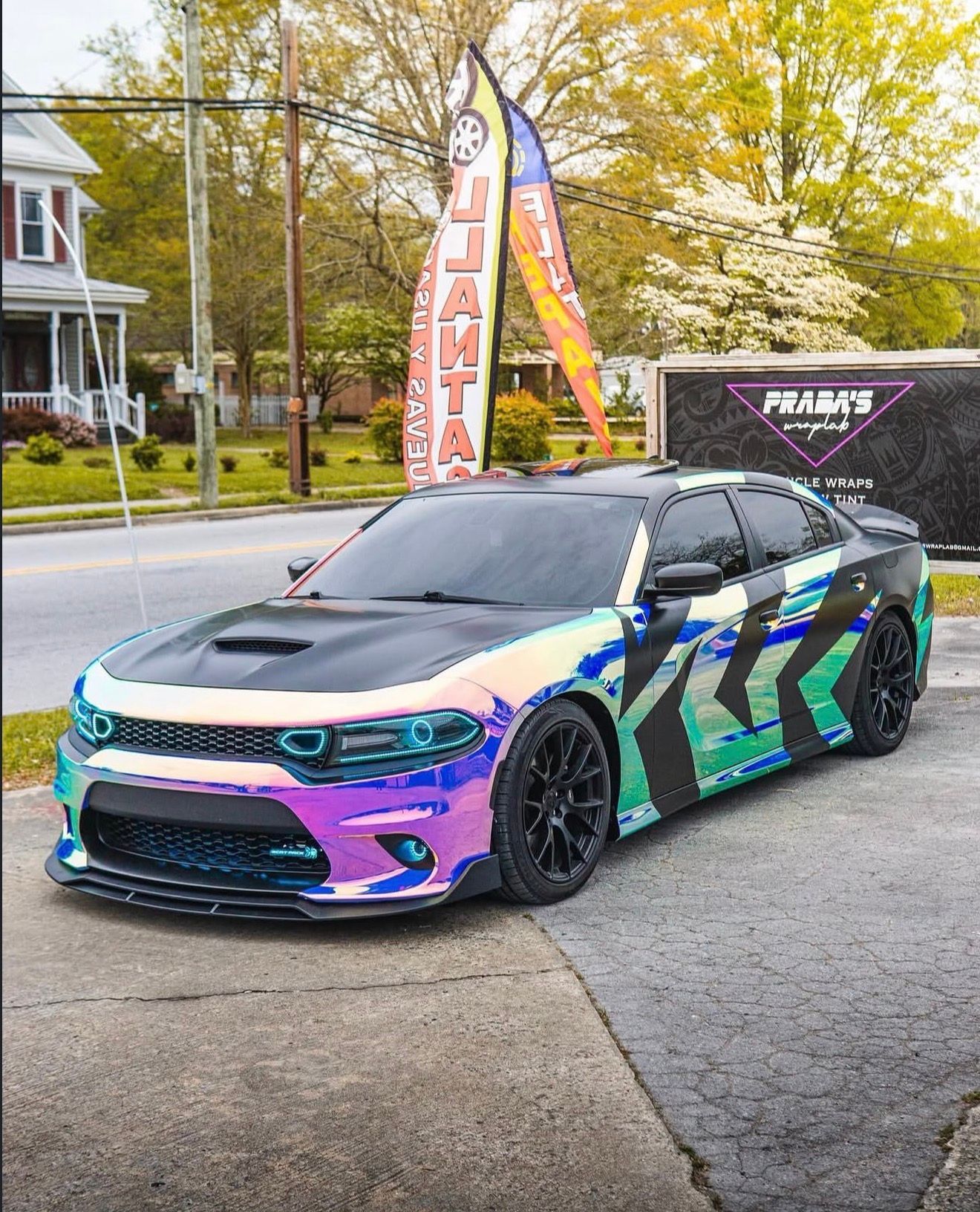 Custom iridescent sports car with black wheels parked outdoors near a dealership banner.