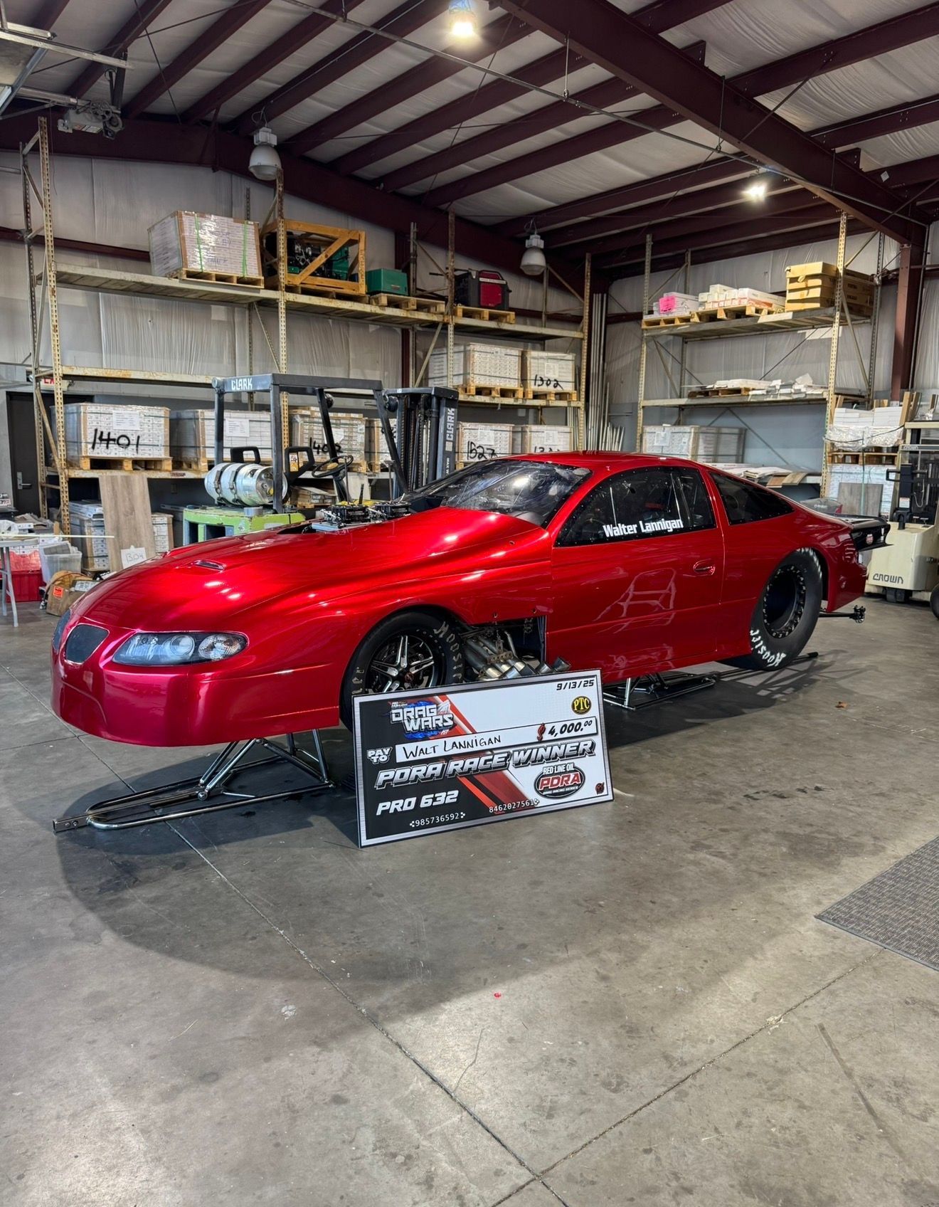 Red sports car in a garage workshop with a sign in front of it.