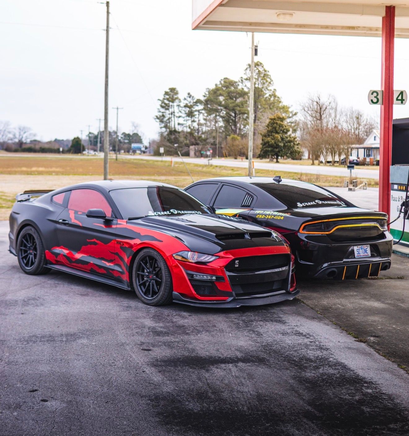 Two customized sports cars, black with red accents and black with gold accents, parked at a gas station.