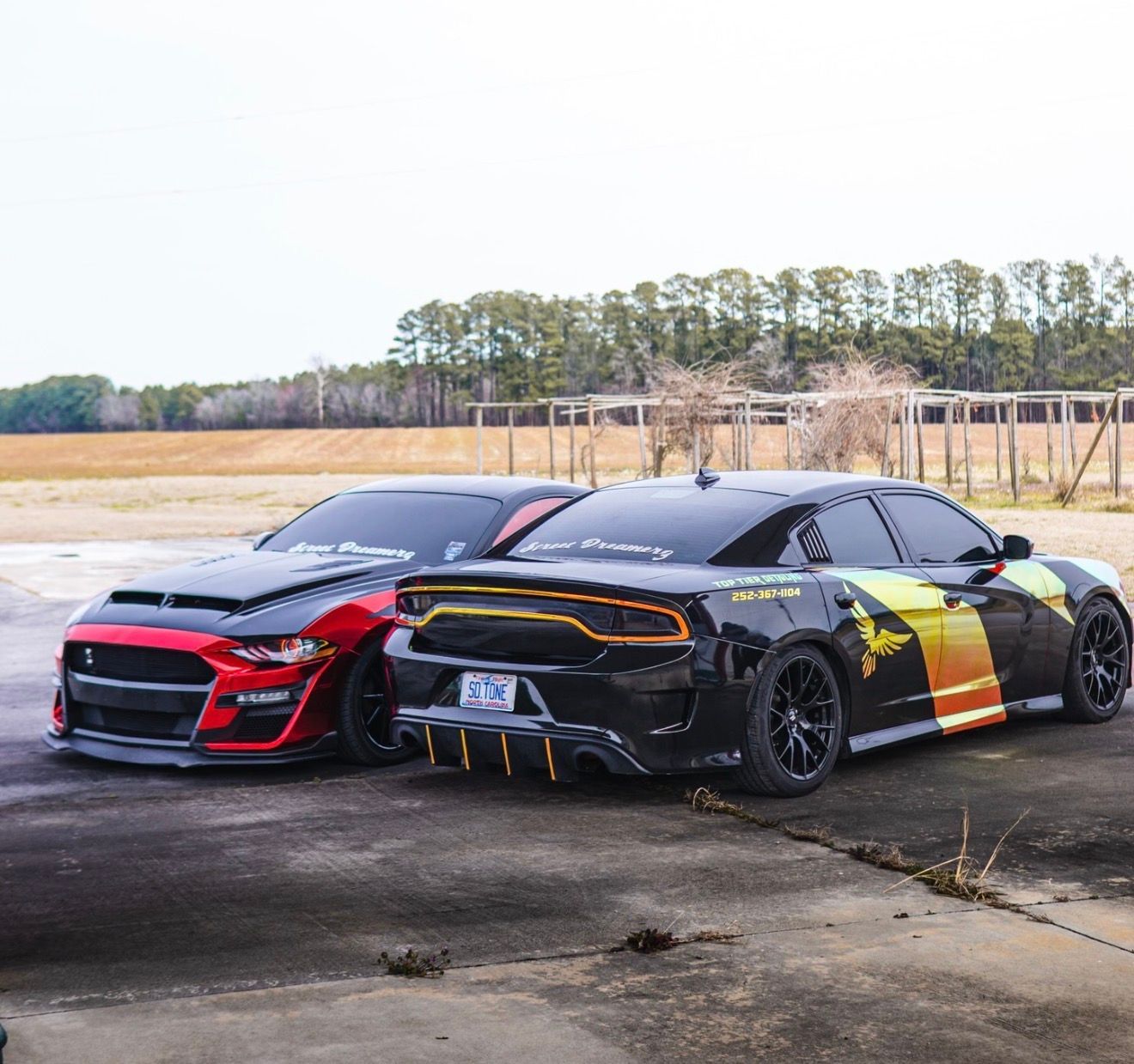 Two customized sports cars parked side by side on a concrete lot, one black and red, one black with yellow accents.