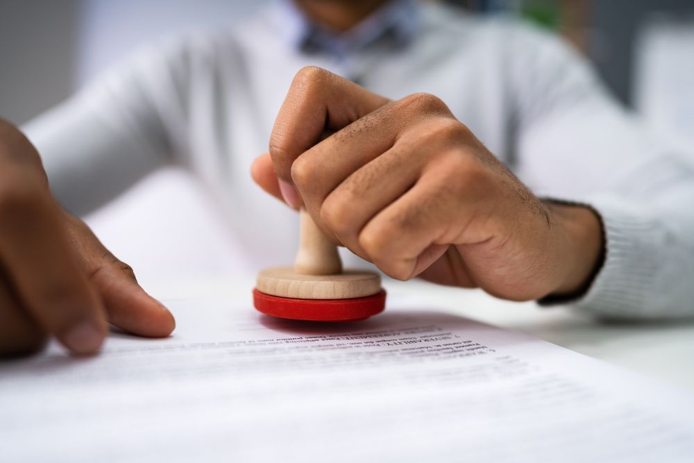 Person stamping a document with a red stamp, hands in focus over paperwork.