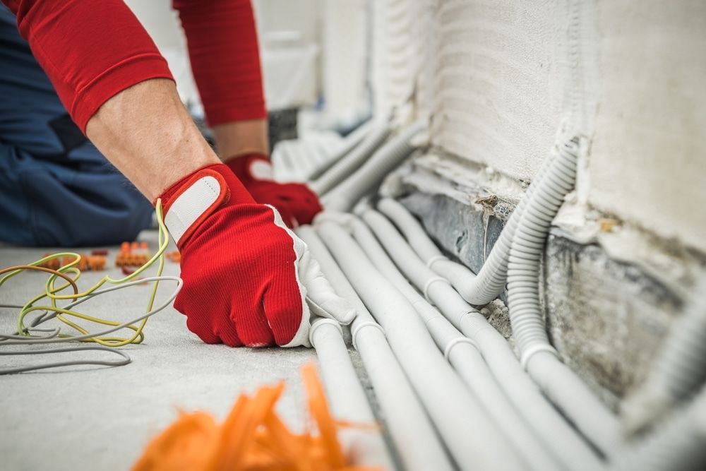 Electrician in Red Gloves Working With Cables Near a Wall — Quaite Electrical Pty Ltd In Woodgate, QLD