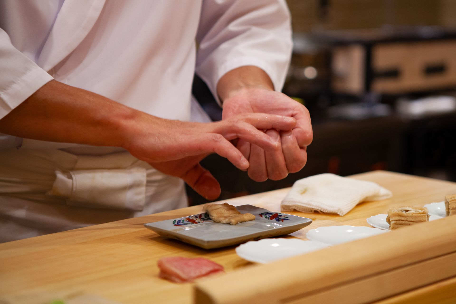 Hands shaping sushi rice on a wooden counter with fish and rice nearby