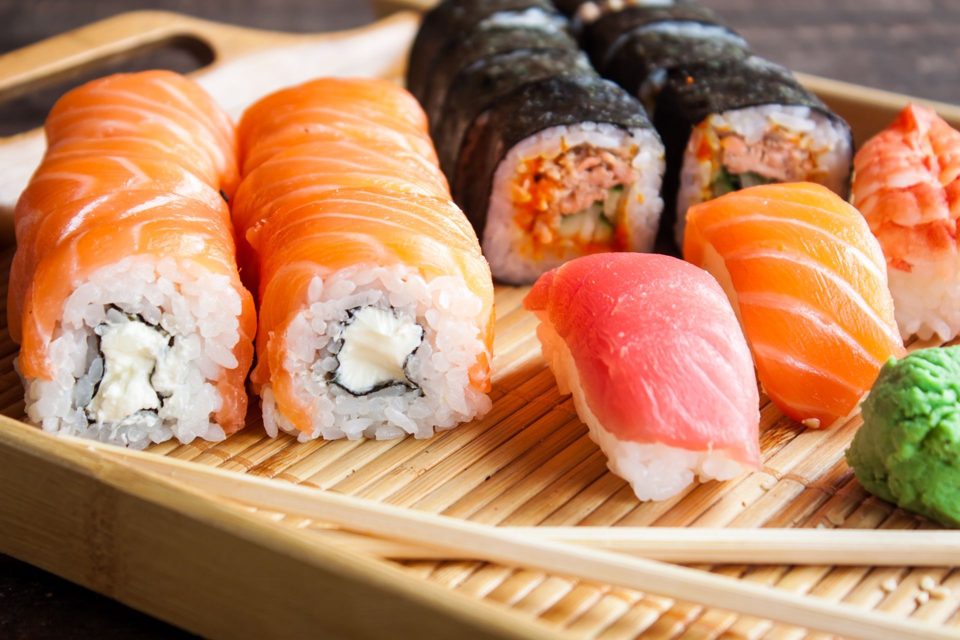 Assorted sushi rolls and nigiri on a bamboo tray, including salmon, tuna, and wasabi, with chopsticks nearby