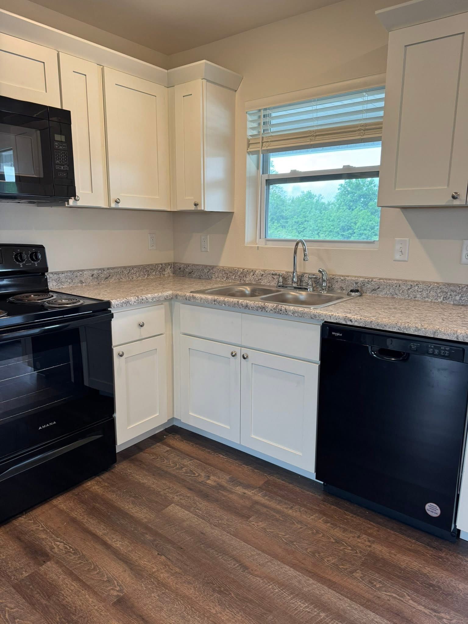 Kitchen with white cabinets, black appliances, granite countertops, and a window.