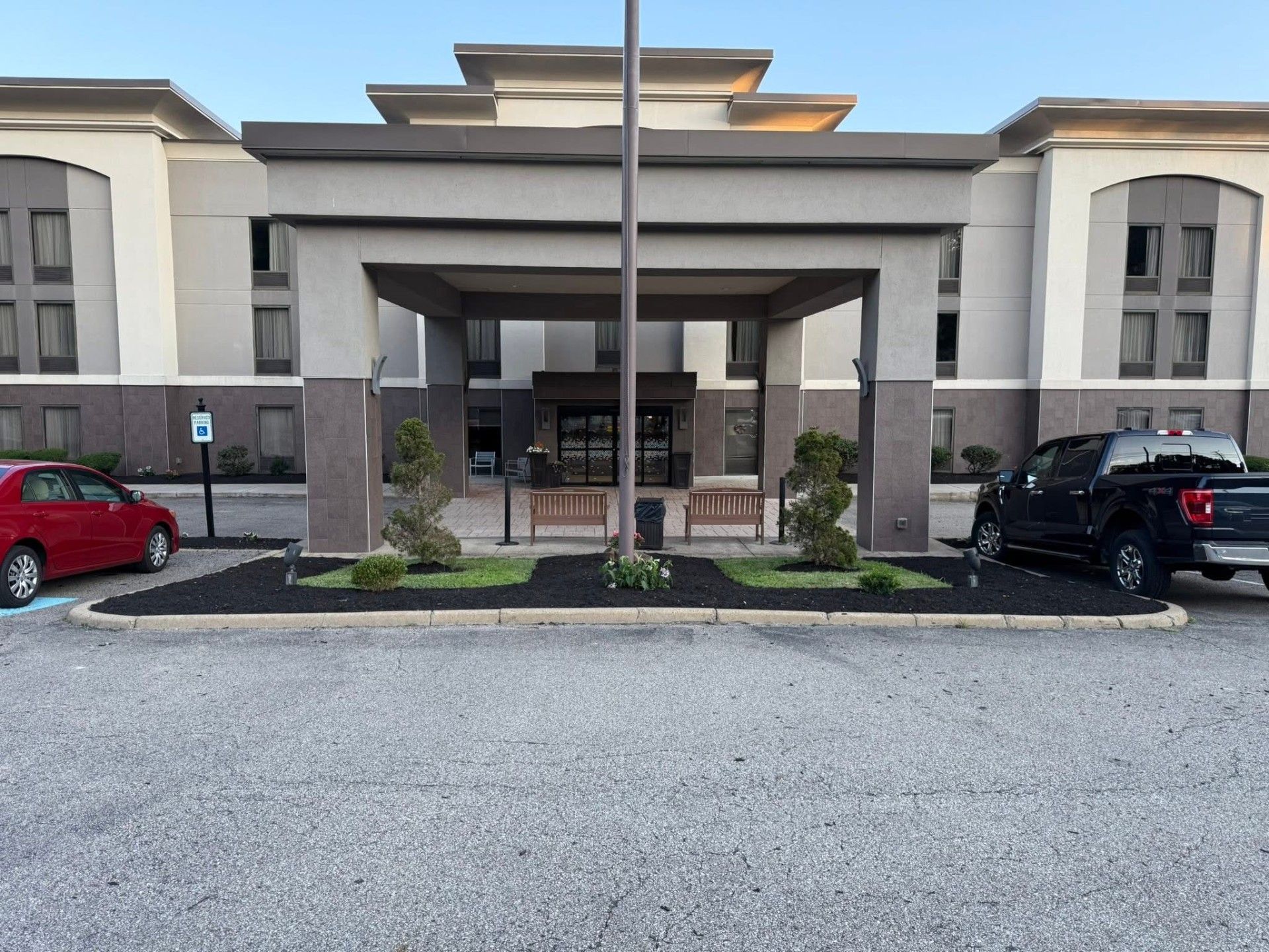 Apartment building exterior with tree, shrubs, and empty paved street in front