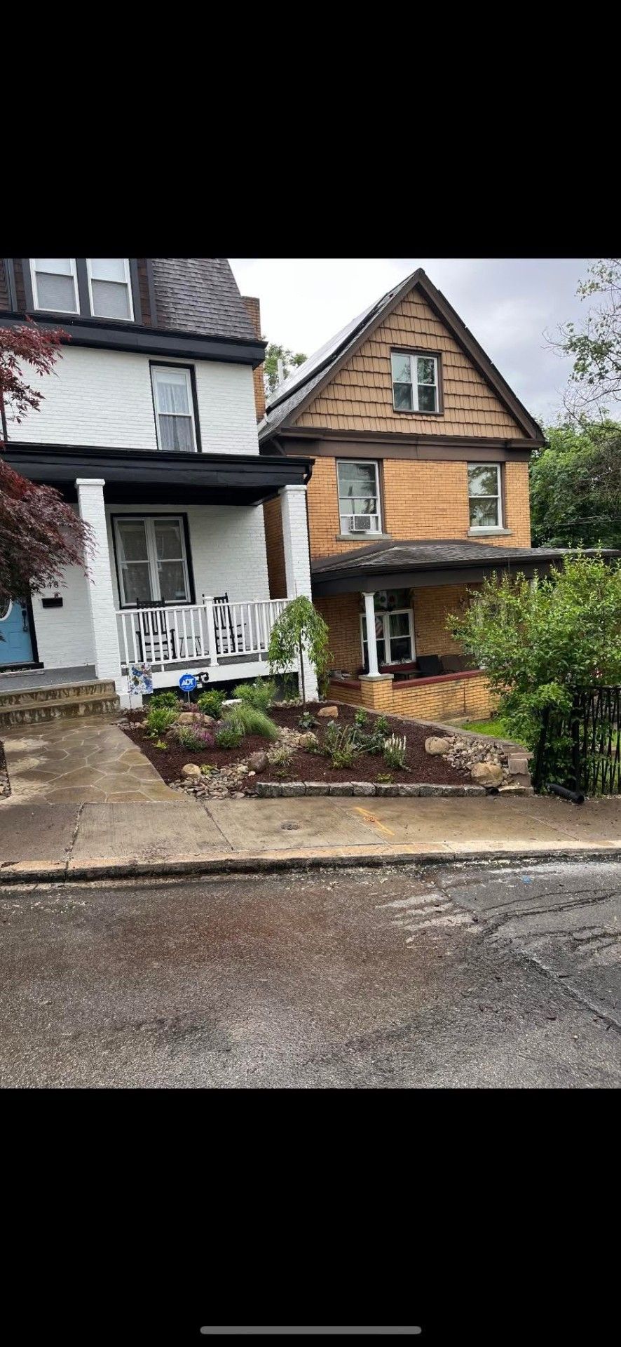 Apartment building exterior with tree, shrubs, and empty paved street in front