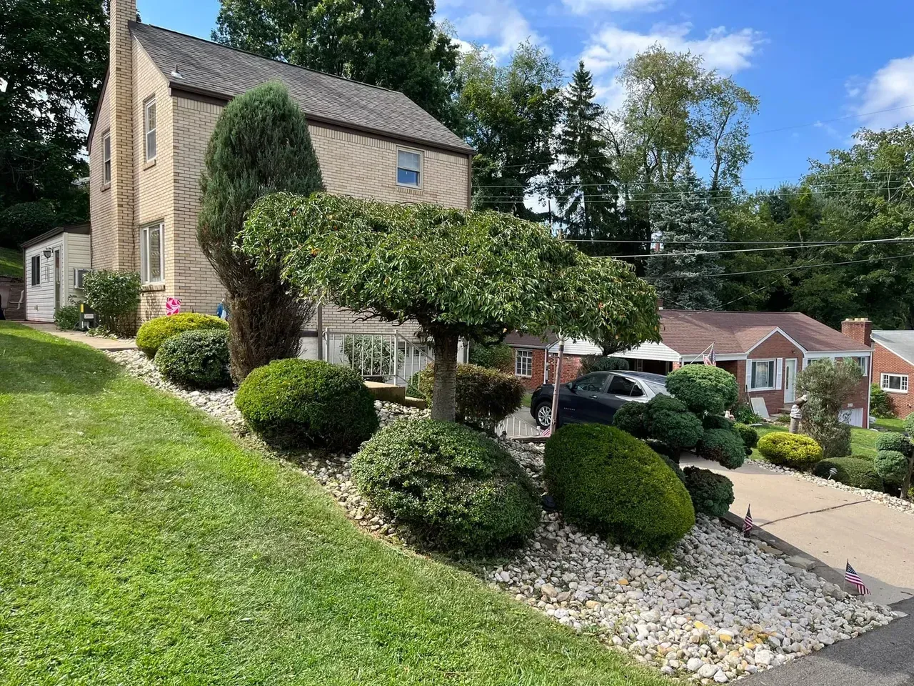 Beige house with landscaped yard, shrubs, and stone groundcover on a sunny day.