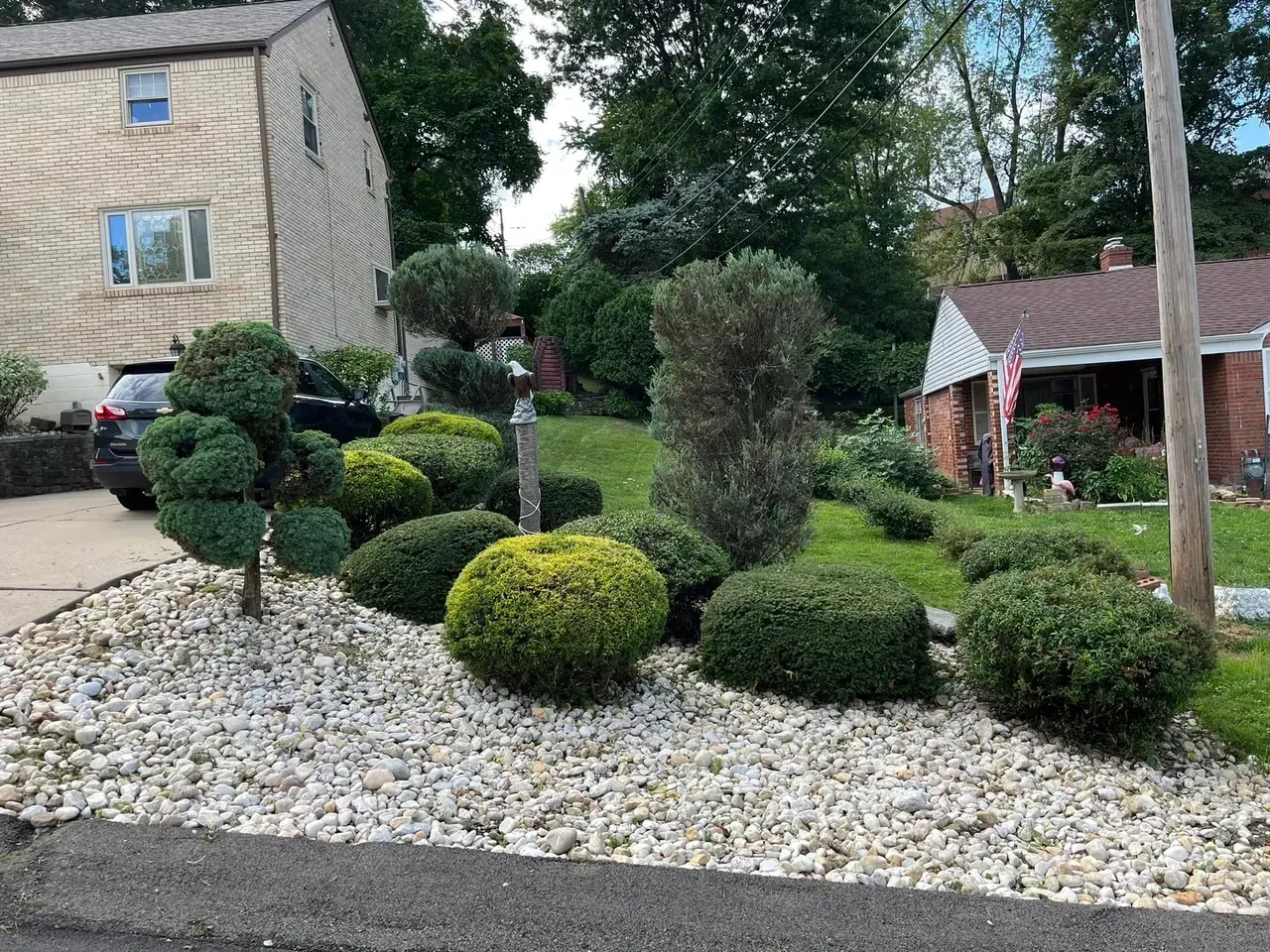 A well-manicured front yard with stone-covered ground, shrubs, and a house in the background.