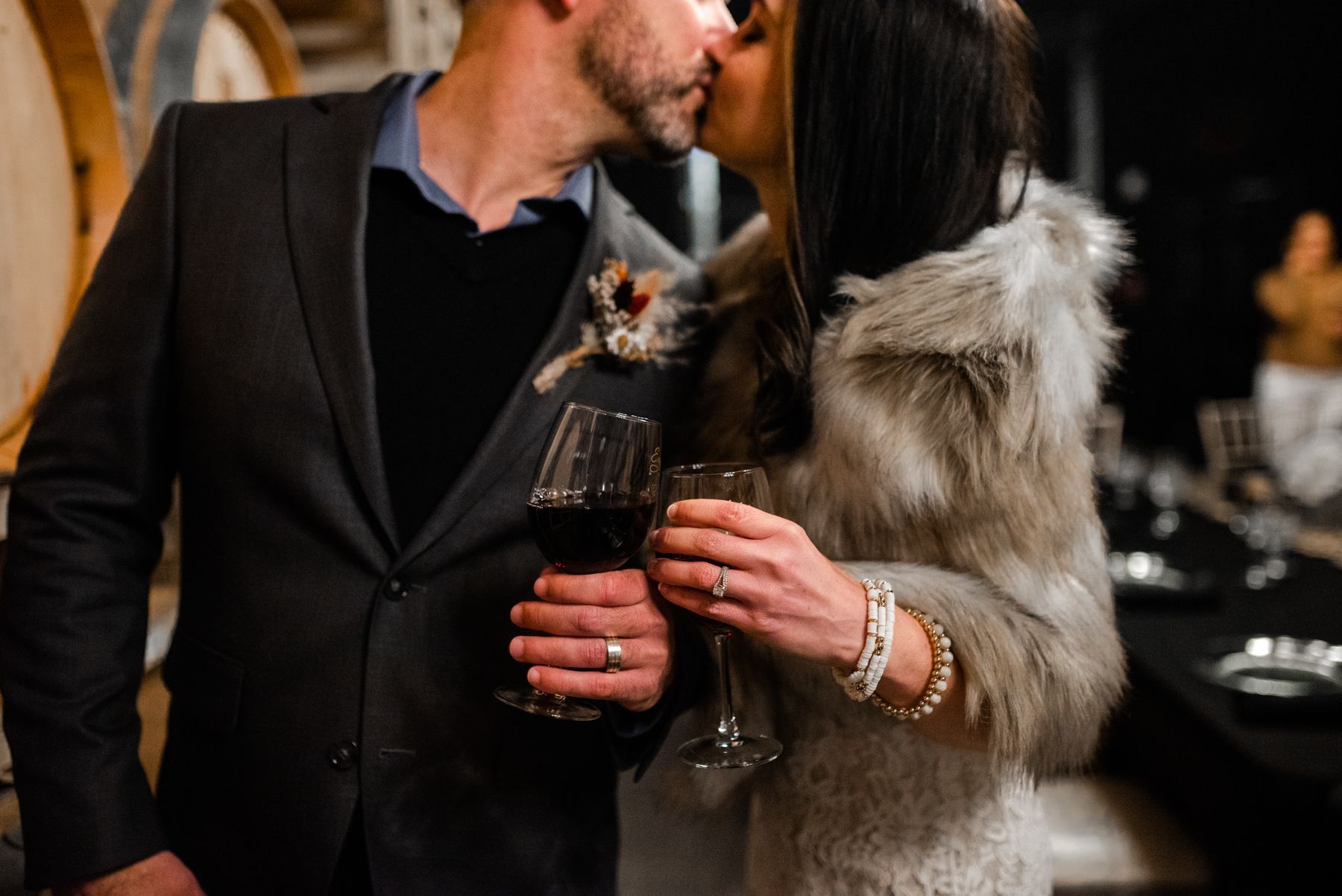 A man and a woman are kissing while holding wine glasses.