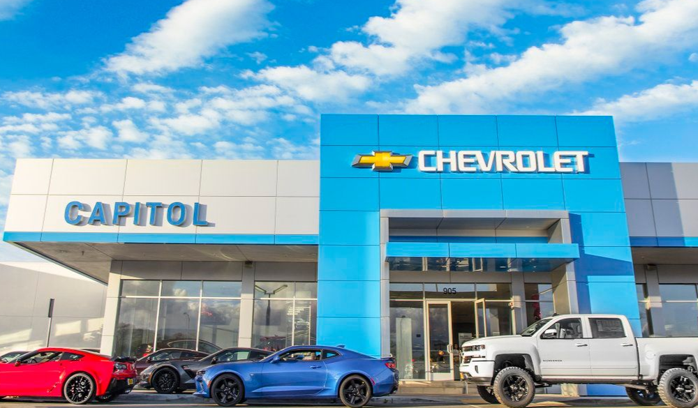 Capitol Chevrolet dealership building with blue and white accents, cars in front, and a cloudy sky.