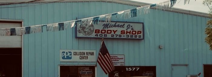 Exterior of Michael's Body Shop, blue building with sign, American flag, and banner.