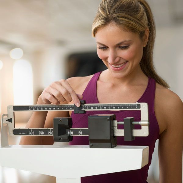 Woman smiling while measuring her weight on a bathroom scale with a black sliding dial
