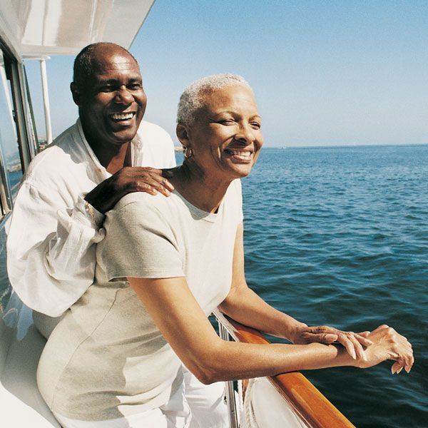 Two people smiling on a boat, leaning over the railing with blue ocean in the background