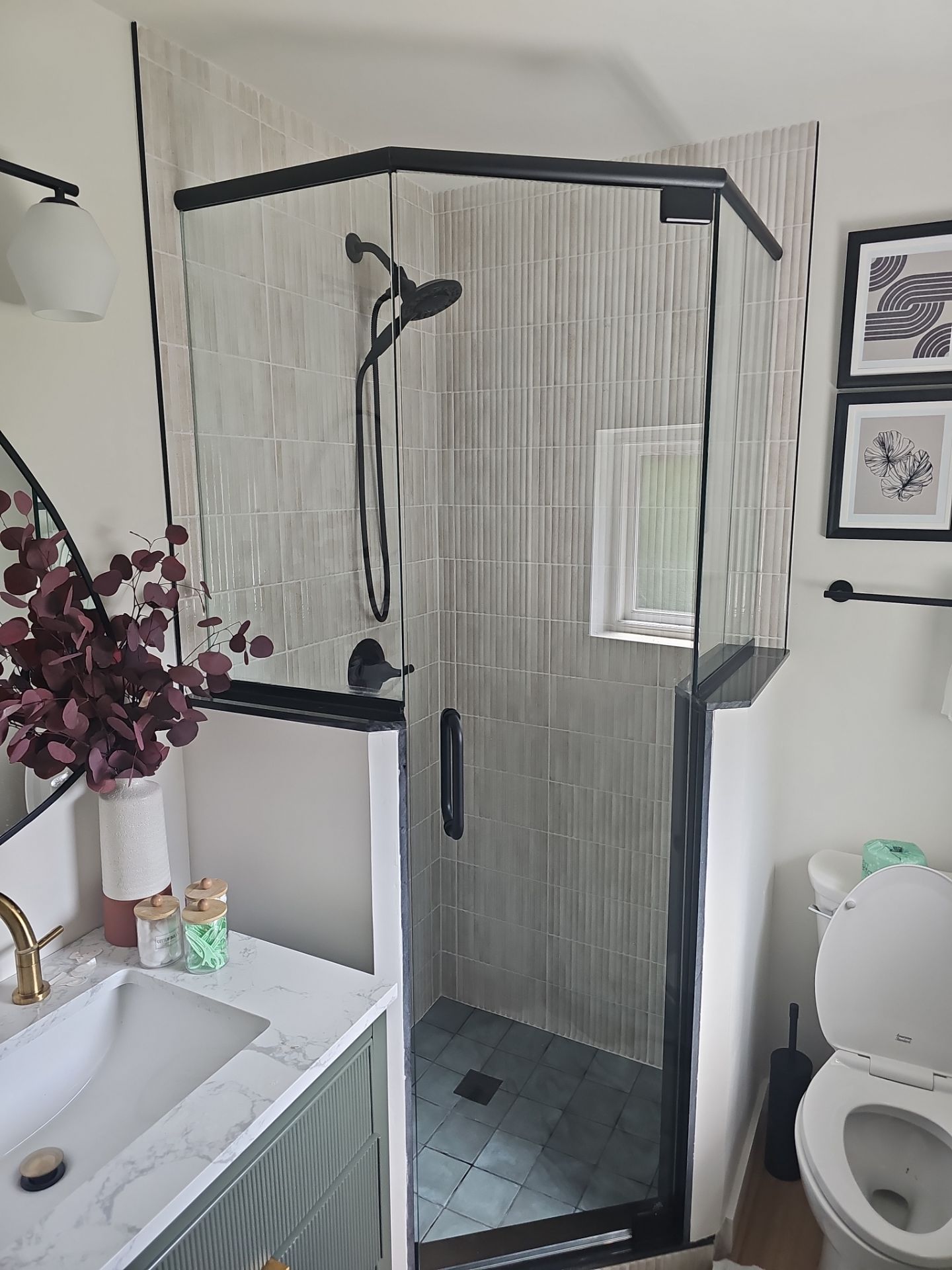 Small bathroom with glass shower, white toilet, and sink with flowers on the counter.