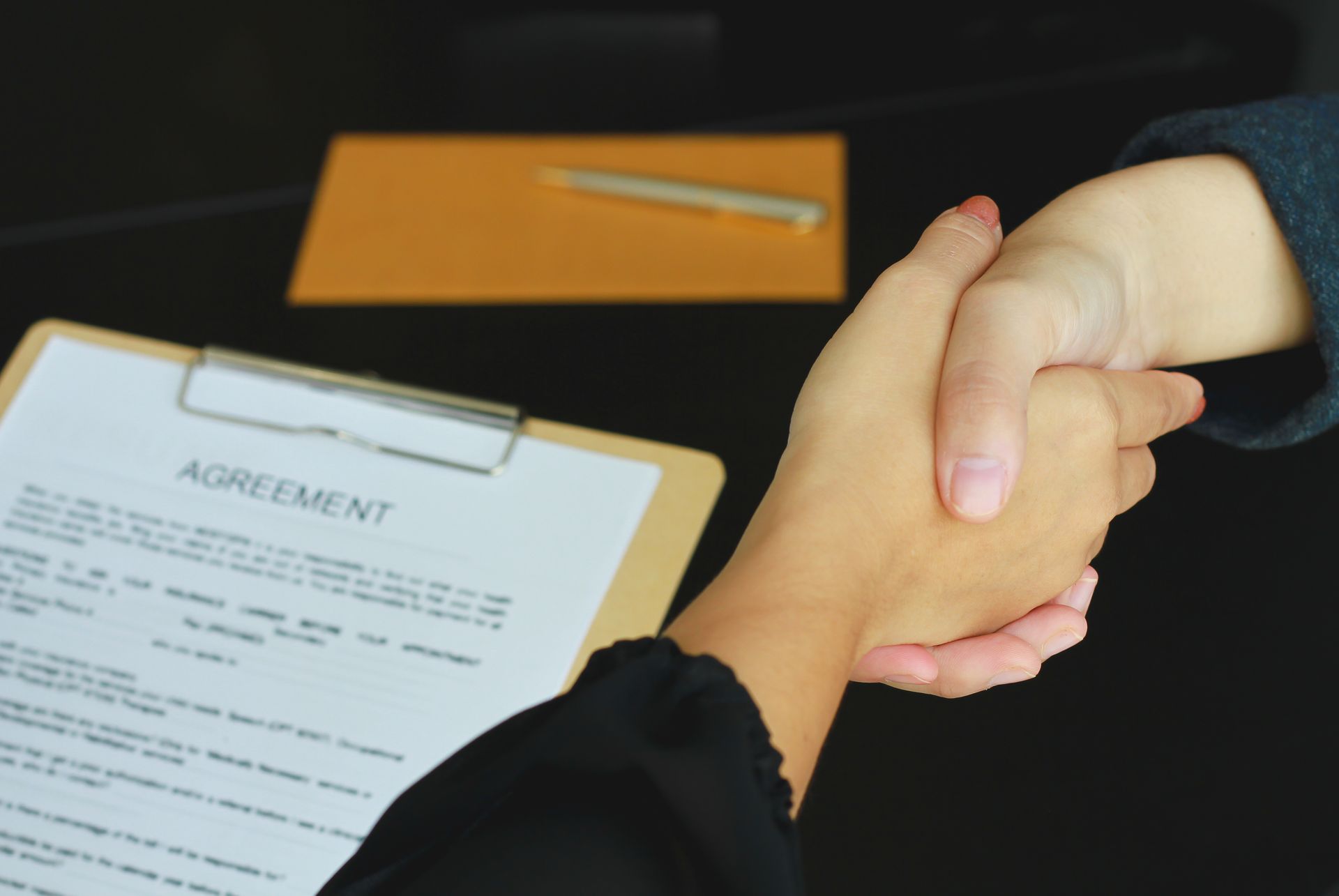 Handshake over an agreement document on a table, signifying a business deal.
