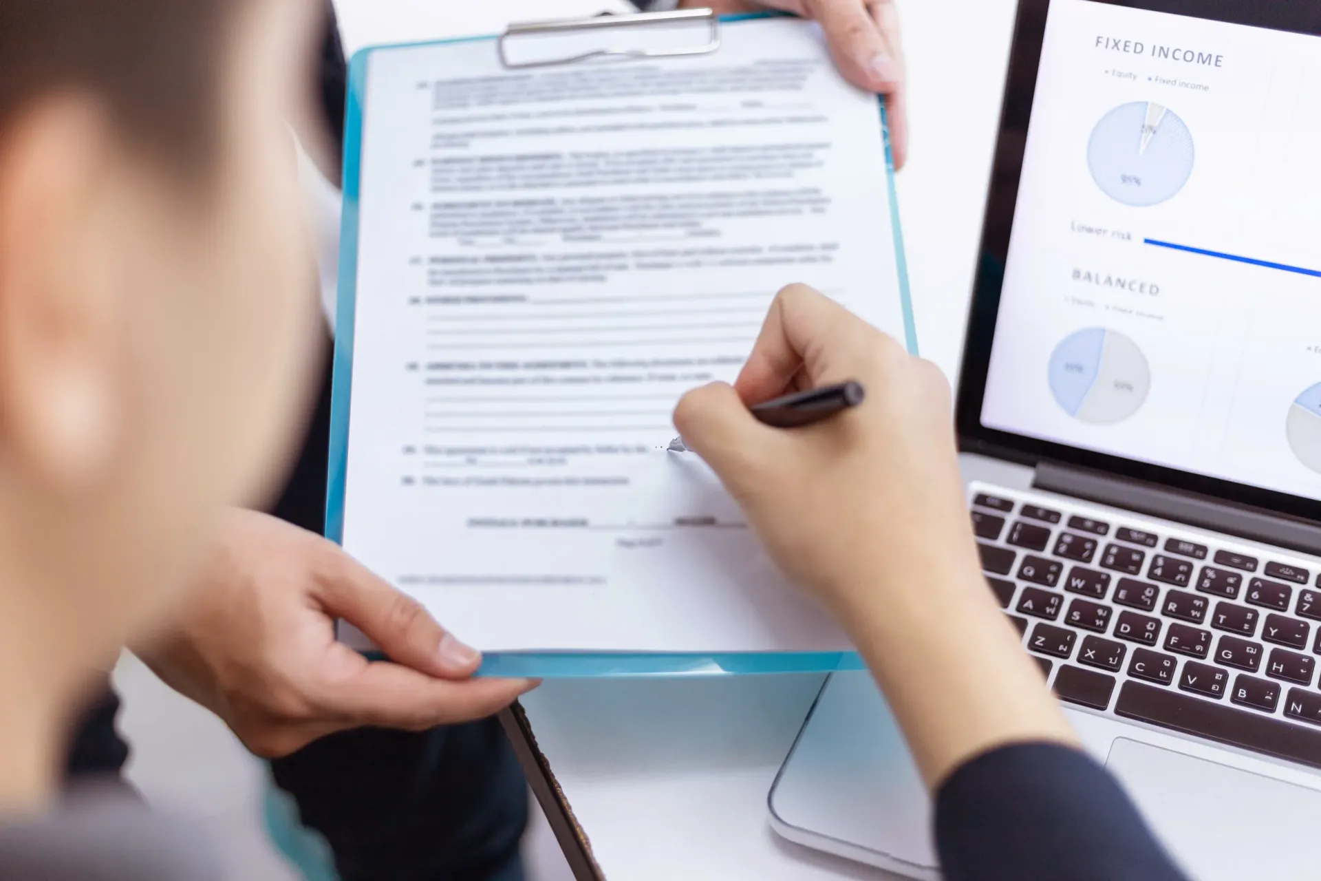 Person reviewing a document beside a laptop with charts on the screen