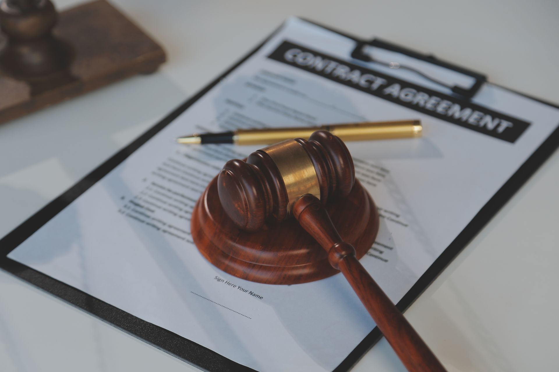 Gavel on a wooden block rests on a contract agreement with a gold pen, suggesting legal or business context.