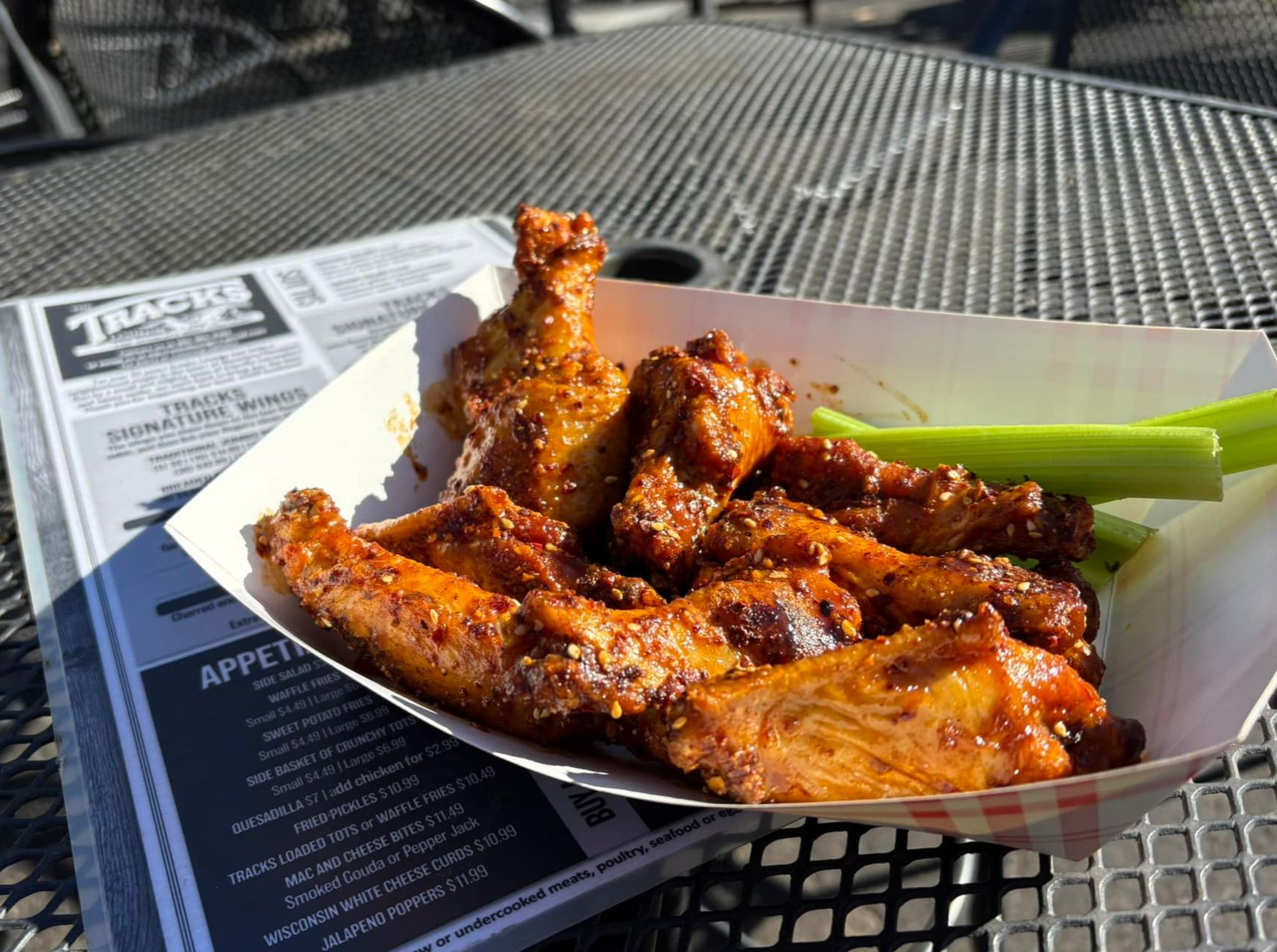 Basket of saucy chicken wings on a table with a celery stick garnish