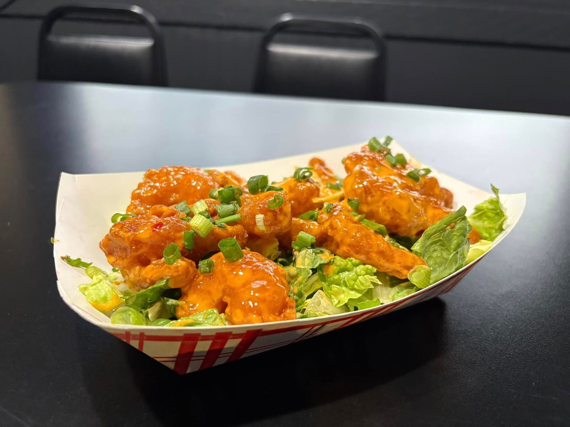 Takeout tray of saucy orange chicken over lettuce with chopped green onions on a table