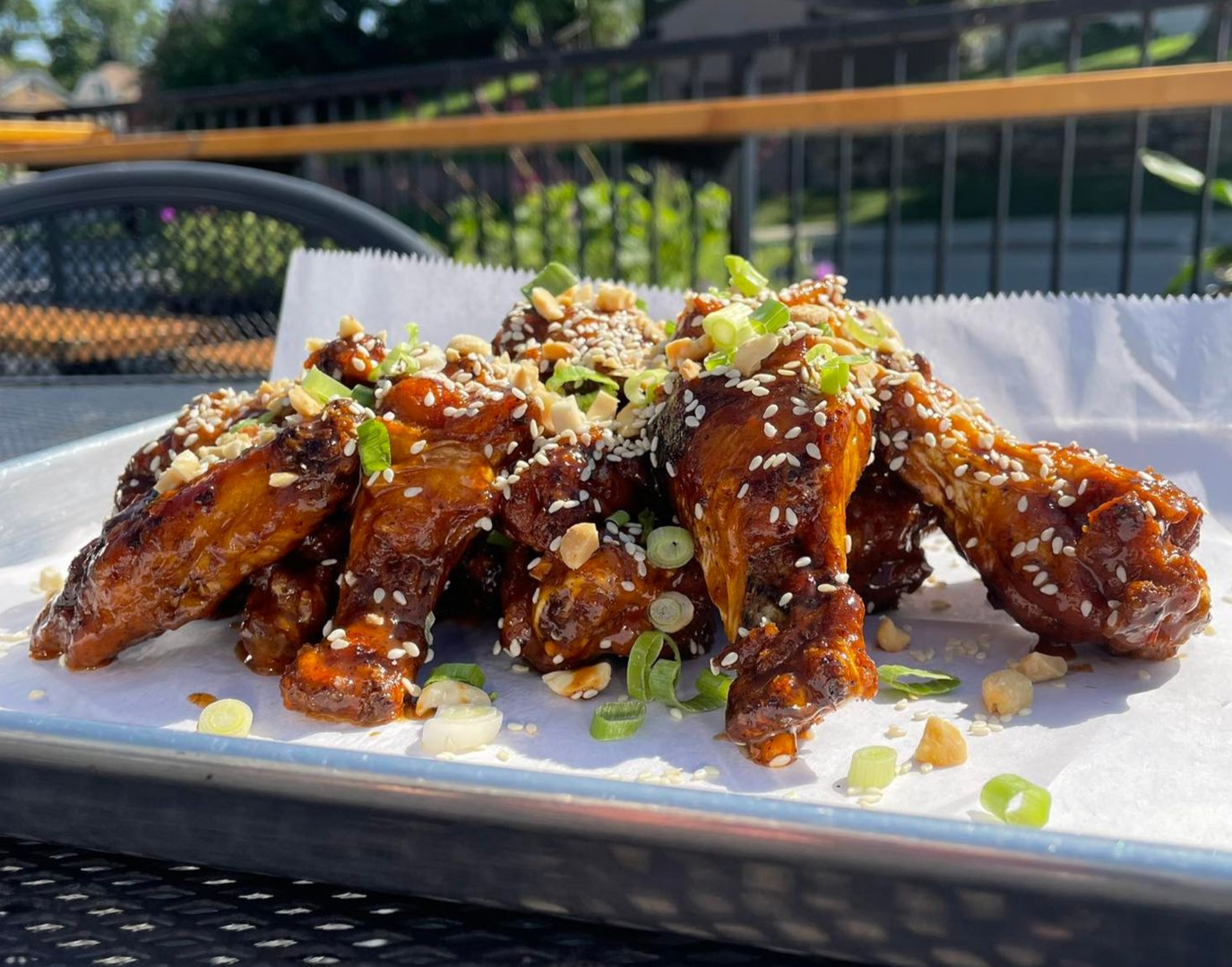 Plate of glazed chicken wings topped with chopped green onions on a white platter outdoors