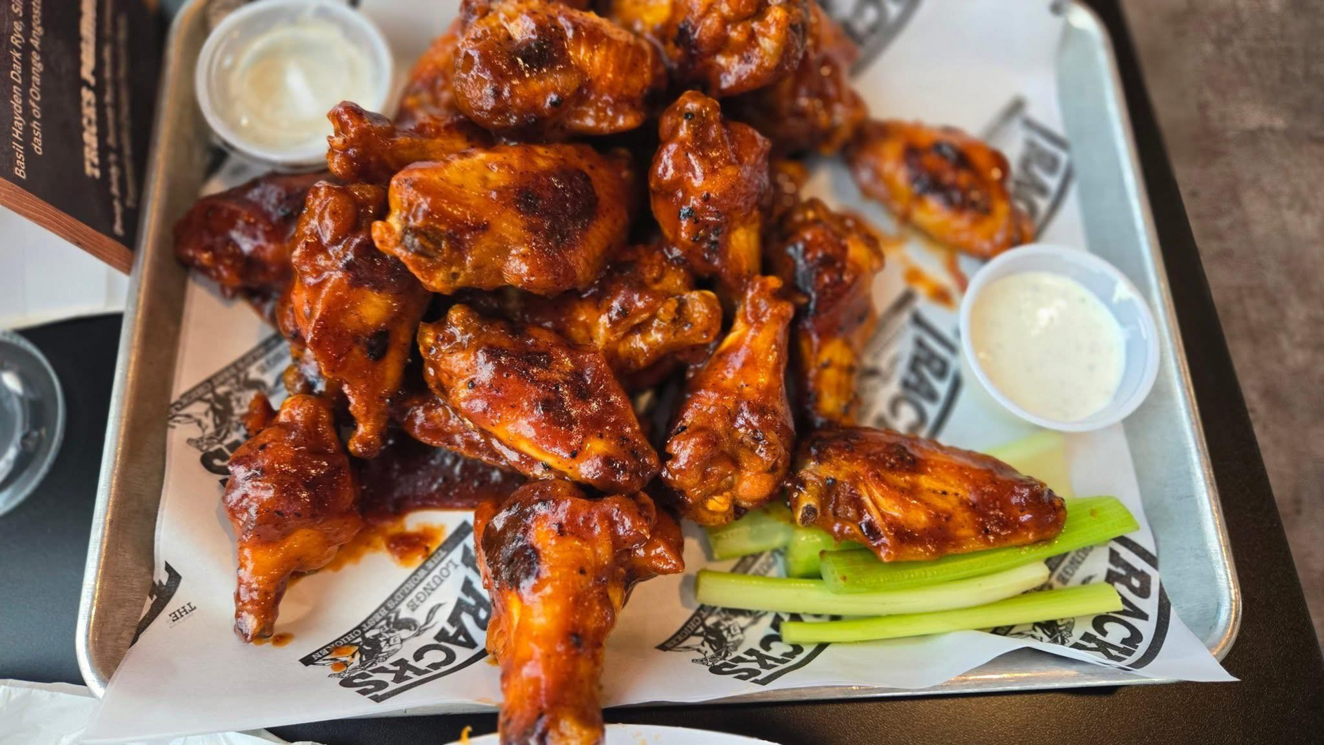 Tray of glazed chicken wings with dipping sauce and celery sticks on restaurant paper liner