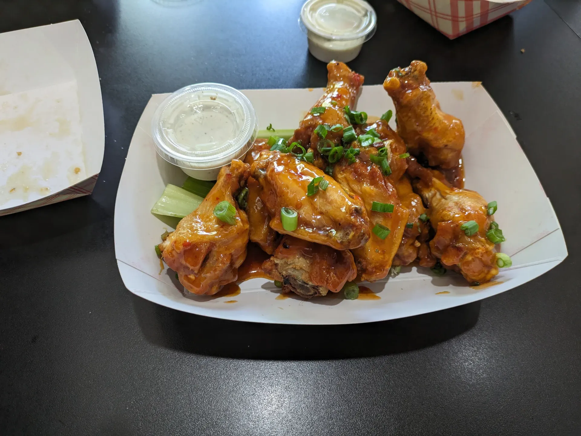 Plate of saucy chicken wings with green garnish and dipping sauces on a restaurant table