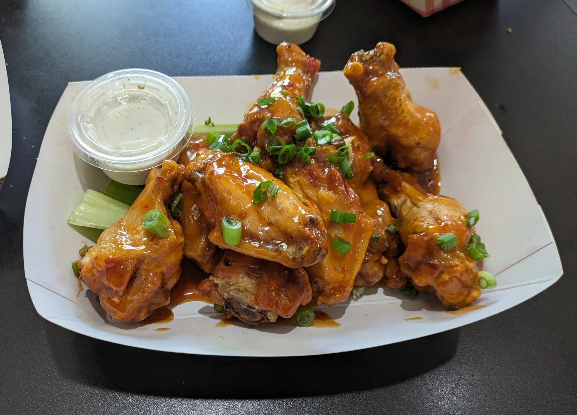 Buffalo chicken wings garnished with green onions on a white plate, with dipping sauce on the side