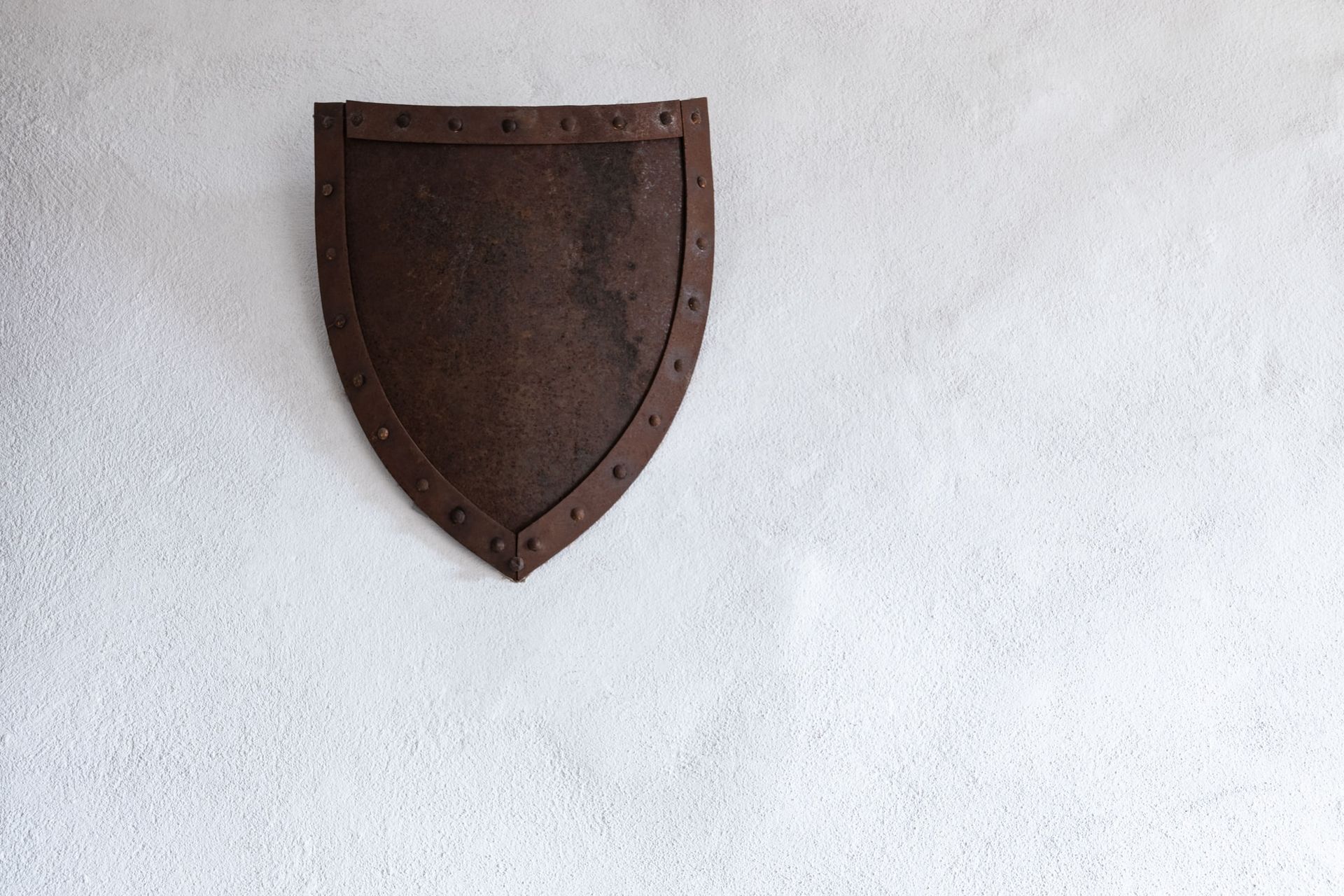 A rusty shield is hanging on a white wall.