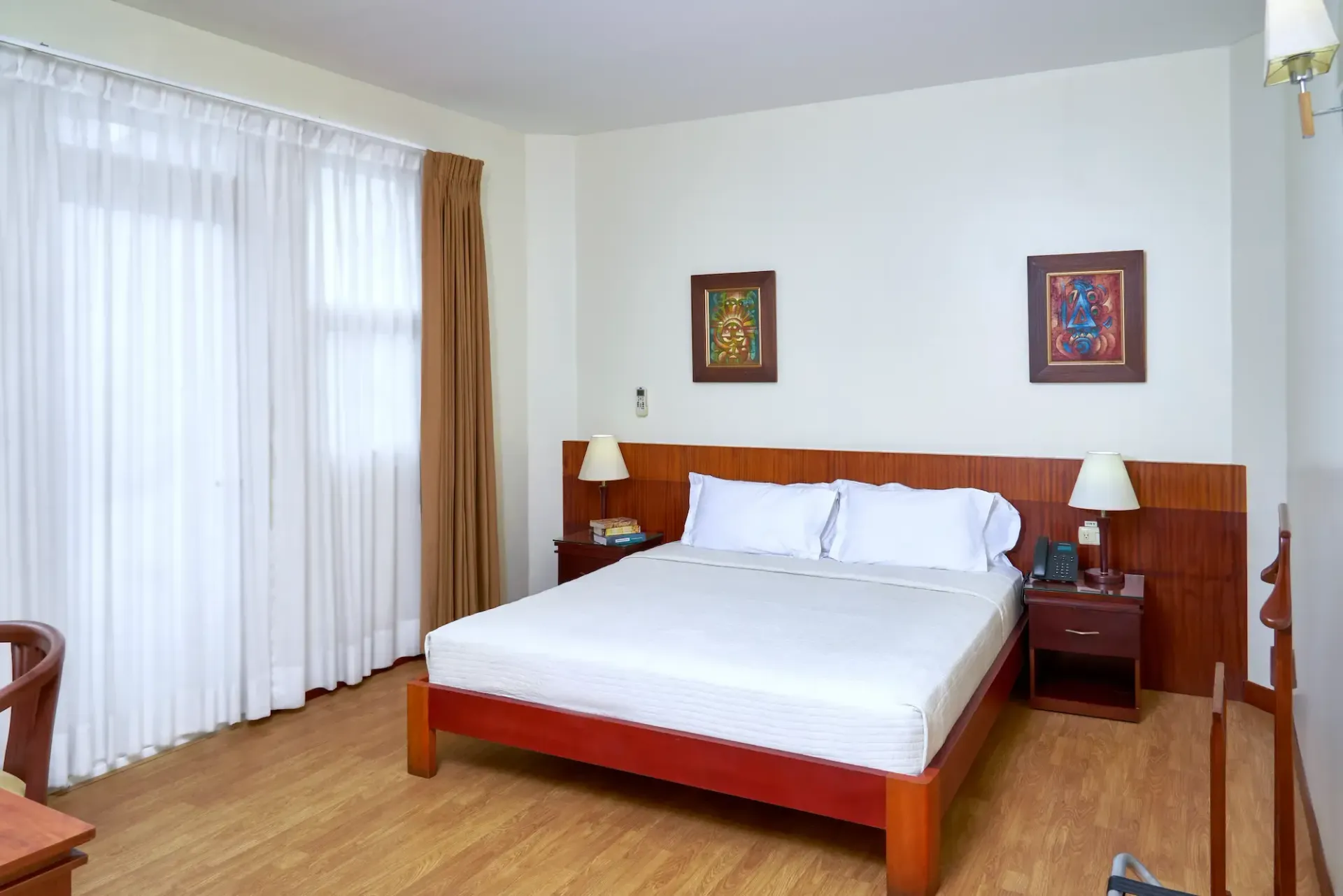 A hotel room with a king size bed , two nightstands , lamps and curtains.