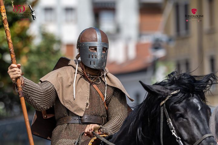 Cavallo nero impennato mentre il cavaliere con la camicia blu si regge sulla sua schiena, sopra uno sgabello rosso all’aperto
