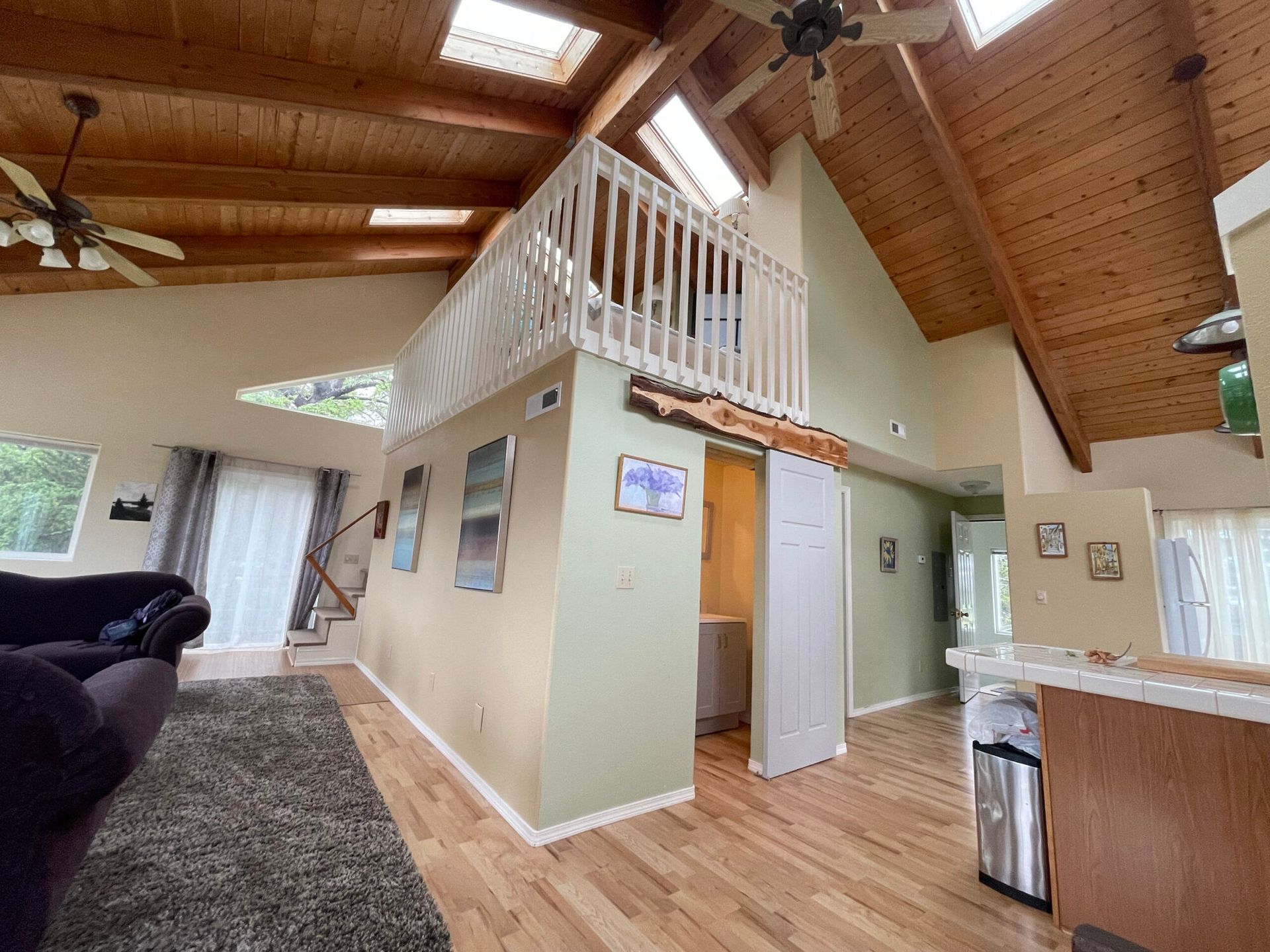 Living room with high vaulted wood ceilings, a loft balcony, light wood floors, and a couch in the foreground.