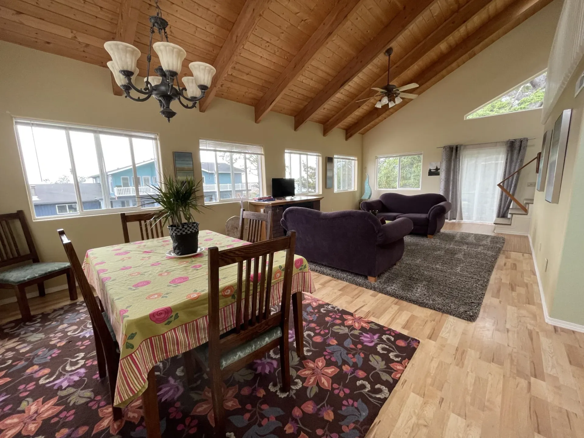 A spacious, open-concept living and dining area with vaulted wood ceilings, neutral walls, and a floral area rug.