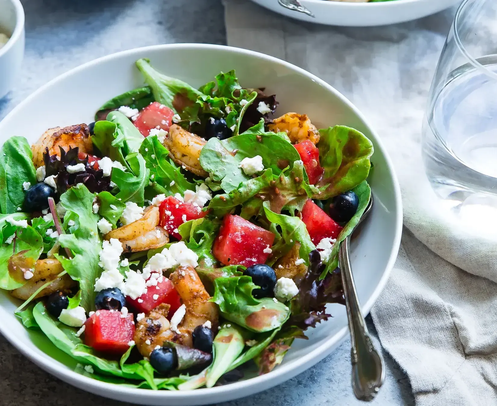 A fresh summer salad with shrimp, cubed watermelon, blueberries, and crumbled feta cheese served in a white bowl.