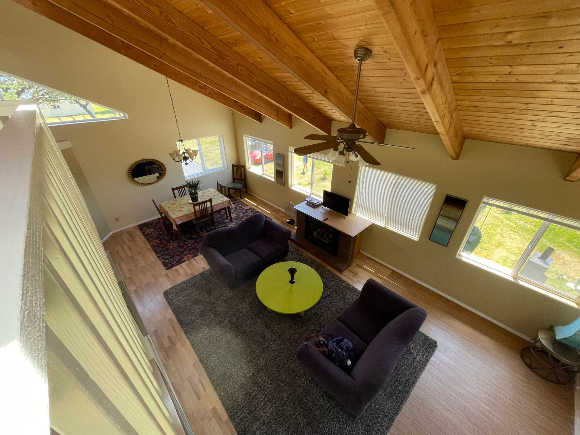 High-angle view of a living and dining area with vaulted wood ceilings, neutral walls, and a large grey area rug.