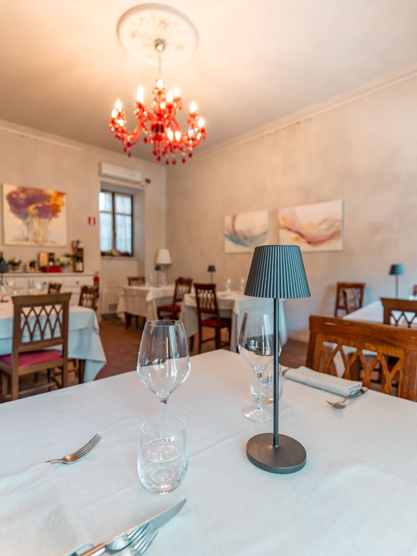 Elegante sala da pranzo con tovaglie bianche, sedie in legno e un lampadario rosso.