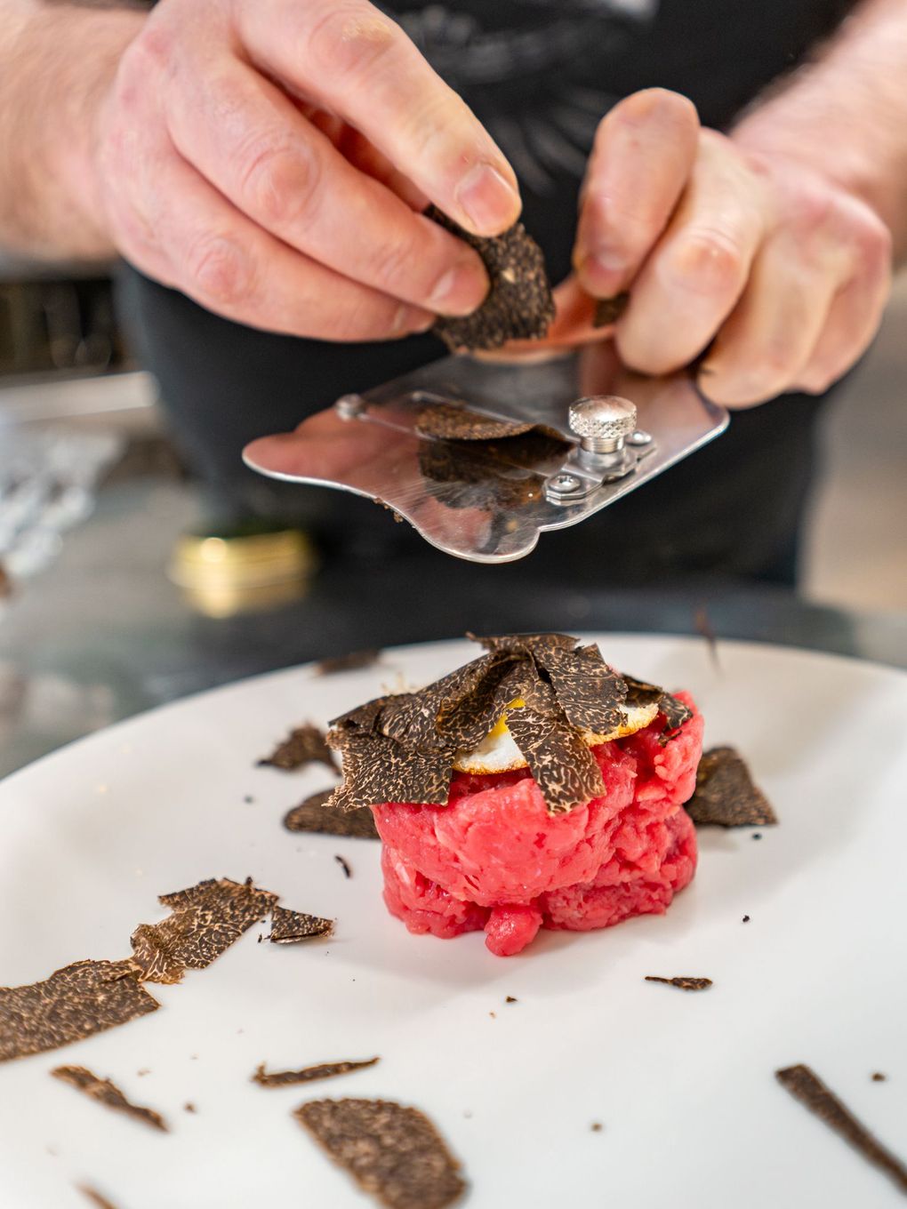 Lo chef dispone delle scaglie di tartufo nero su un piatto rosso brillante adagiato su un piatto bianco.